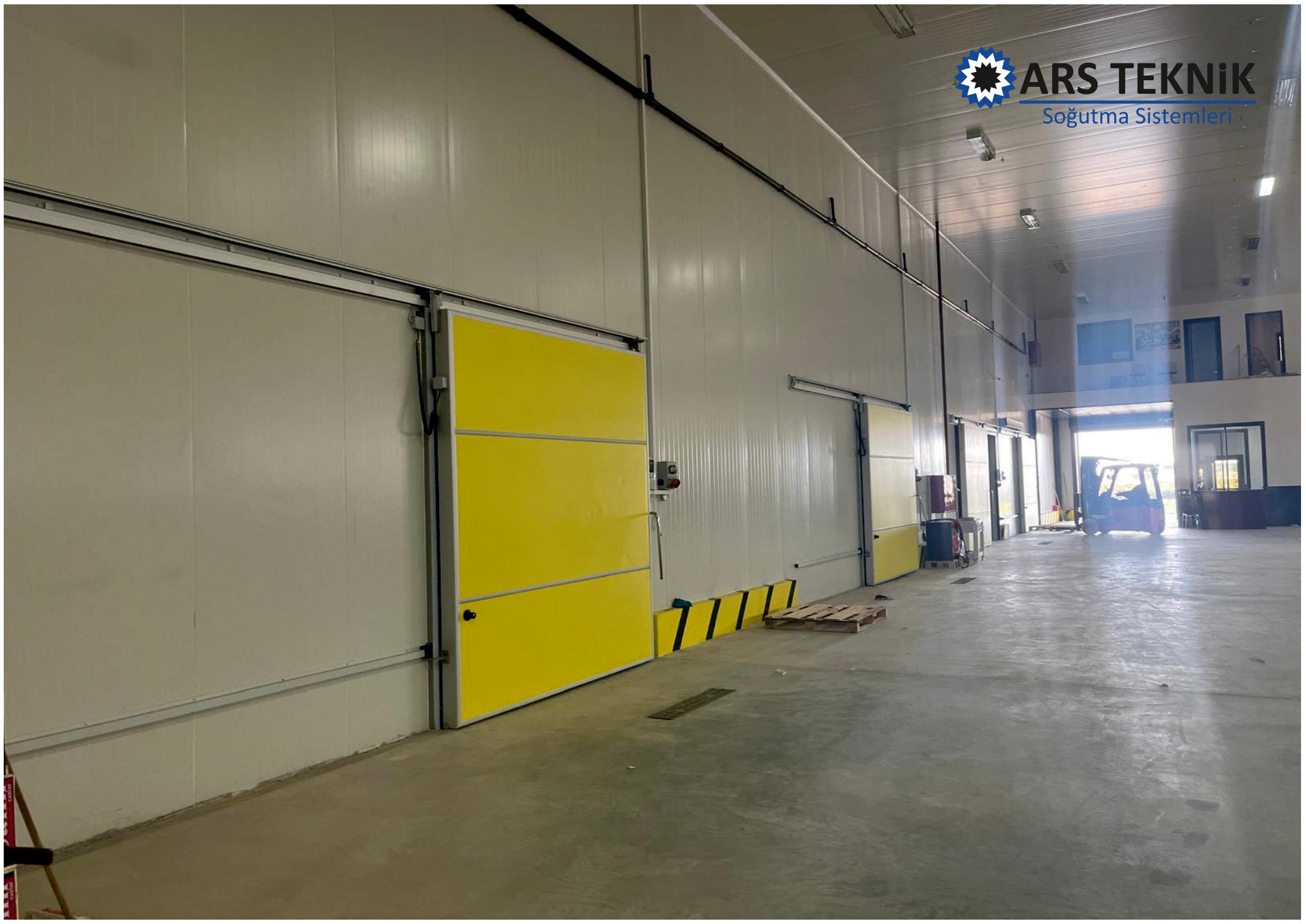 A large hall with white insulated wall panels and yellow sliding doors.