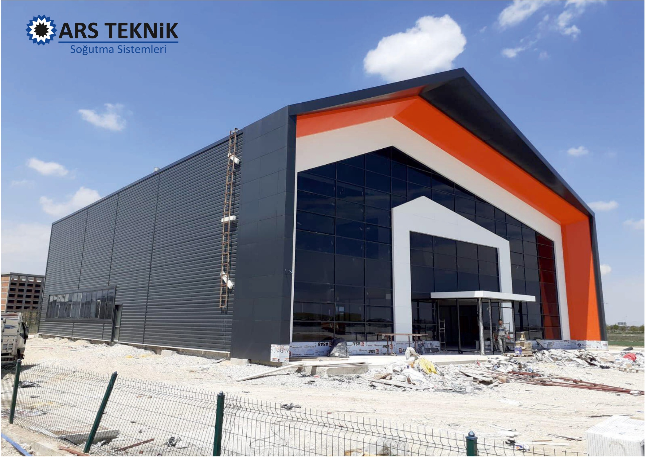 A dark panel-clad industrial building with a glazed gable end.