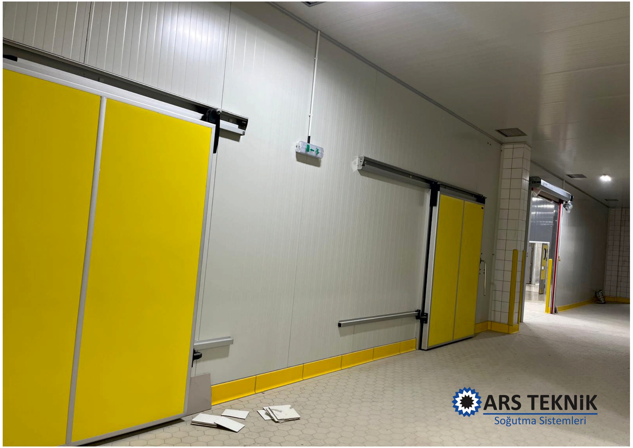 A corridor with white wall panels and yellow sliding doors.