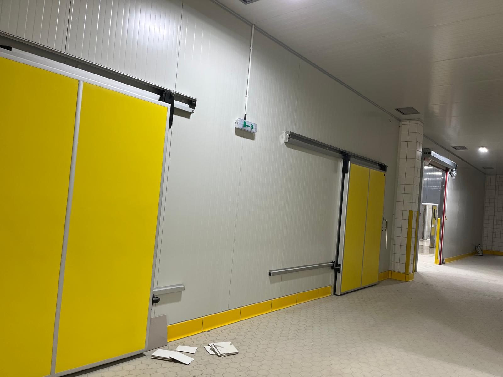 A corridor with white wall panels and yellow sliding doors.